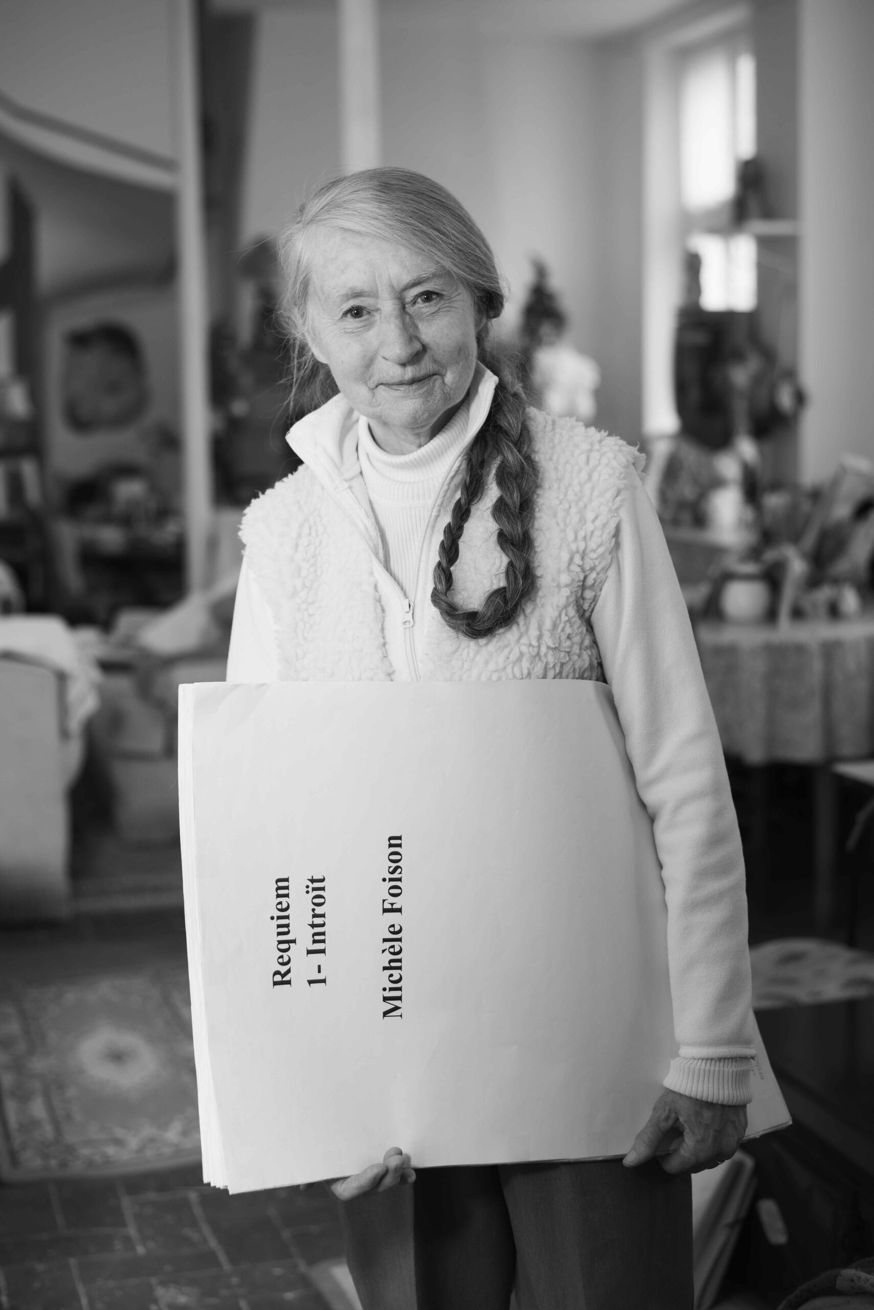 Michèle Foison se tient debout au milieu de son salon et tient la gigantesque partition de son requiem dans les bras